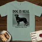 Dog is Real Rottweiler T-Shirt flat lay in Bay, featuring Black halftone newspaper photo of a Rottweiler standing in profile with head turned to the camera, under the headline DOG IS REAL, with the caption Praise Be to Dog. Woof..