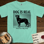 Dog is Real Rottweiler T-Shirt flat lay in Island Reef, featuring Black halftone newspaper photo of a Rottweiler standing in profile with head turned to the camera, under the headline DOG IS REAL, with the caption Praise Be to Dog. Woof..