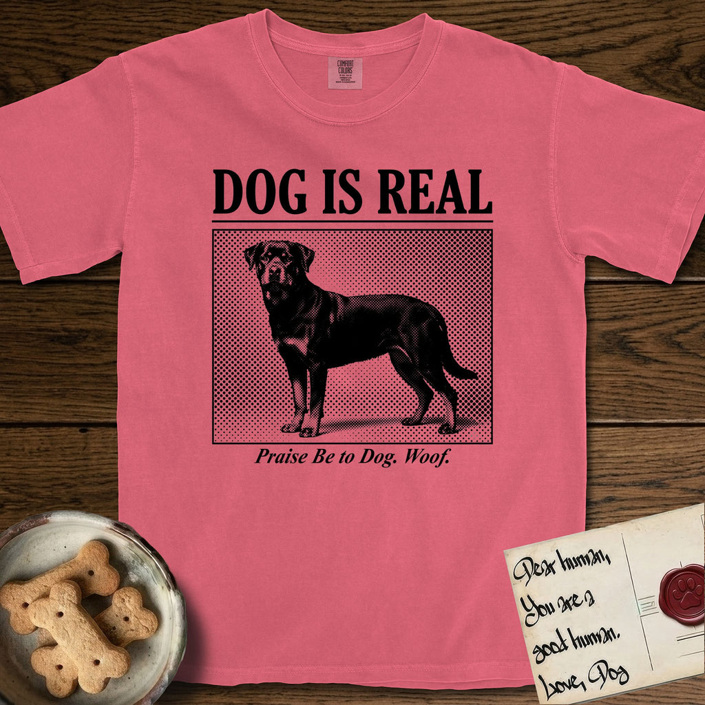 Dog is Real Rottweiler T-Shirt flat lay in Watermelon, featuring Black halftone newspaper photo of a Rottweiler standing in profile with head turned to the camera, under the headline DOG IS REAL, with the caption Praise Be to Dog. Woof..