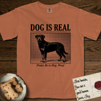 Dog is Real Rottweiler T-Shirt flat lay in Yam, featuring Black halftone newspaper photo of a Rottweiler standing in profile with head turned to the camera, under the headline DOG IS REAL, with the caption Praise Be to Dog. Woof..