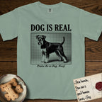Dog is Real Schnauzer T-Shirt flat lay in Bay, featuring Black halftone newspaper photo of a bearded Schnauzer with an upright tail standing in profile with head turned to the camera, under the headline DOG IS REAL, with the caption Praise Be to Dog. Woof..