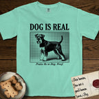 Dog is Real Schnauzer T-Shirt flat lay in Island Reef, featuring Black halftone newspaper photo of a bearded Schnauzer with an upright tail standing in profile with head turned to the camera, under the headline DOG IS REAL, with the caption Praise Be to Dog. Woof..