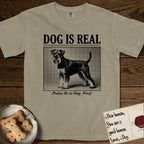 Dog is Real Schnauzer T-Shirt flat lay in Khaki, featuring Black halftone newspaper photo of a bearded Schnauzer with an upright tail standing in profile with head turned to the camera, under the headline DOG IS REAL, with the caption Praise Be to Dog. Woof..