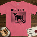 Dog is Real Schnauzer T-Shirt flat lay in Watermelon, featuring Black halftone newspaper photo of a bearded Schnauzer with an upright tail standing in profile with head turned to the camera, under the headline DOG IS REAL, with the caption Praise Be to Dog. Woof..