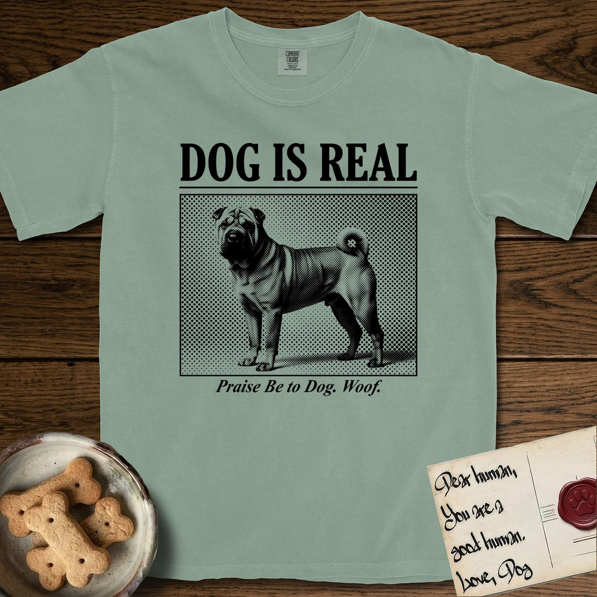 Dog is Real Shar-Pei T-Shirt flat lay in Bay, featuring Black halftone newspaper photo of a wrinkled Shar-Pei with a curled tail standing in profile with head turned to the camera, under the headline DOG IS REAL, with the caption Praise Be to Dog. Woof..