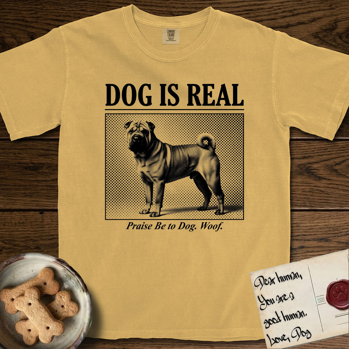Dog is Real Shar-Pei T-Shirt flat lay in Mustard, featuring Black halftone newspaper photo of a wrinkled Shar-Pei with a curled tail standing in profile with head turned to the camera, under the headline DOG IS REAL, with the caption Praise Be to Dog. Woof..