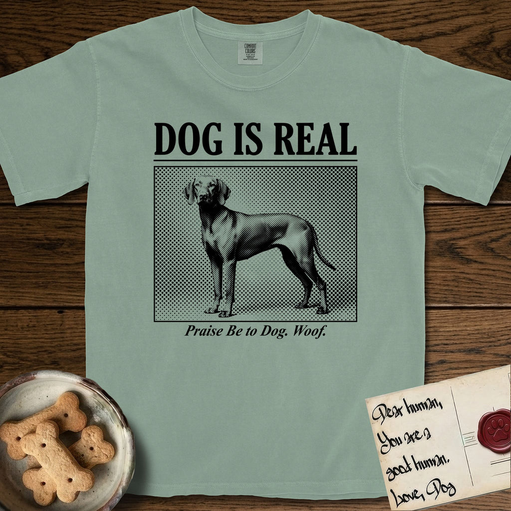 Dog is Real Vizsla T-Shirt flat lay in Bay, featuring Black halftone newspaper photo of a lean Vizsla with long ears standing in profile with head turned to the camera, under the headline DOG IS REAL, with the caption Praise Be to Dog. Woof..