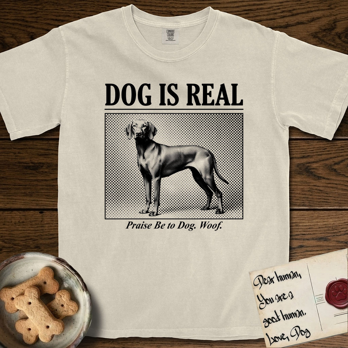 Dog is Real Vizsla T-Shirt flat lay in Ivory, featuring Black halftone newspaper photo of a lean Vizsla with long ears standing in profile with head turned to the camera, under the headline DOG IS REAL, with the caption Praise Be to Dog. Woof..