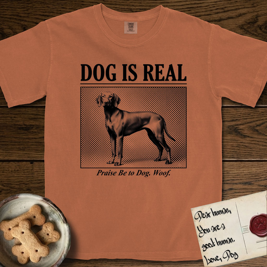 Dog is Real Vizsla T-Shirt flat lay in Yam, featuring Black halftone newspaper photo of a lean Vizsla with long ears standing in profile with head turned to the camera, under the headline DOG IS REAL, with the caption Praise Be to Dog. Woof..
