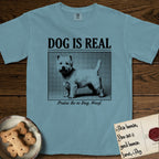 Dog is Real Westie T-Shirt flat lay in Ice Blue, featuring Black halftone newspaper photo of a white Westie with upright ears and tail standing in profile with head turned to the camera, under the headline DOG IS REAL, with the caption Praise Be to Dog. Woof..