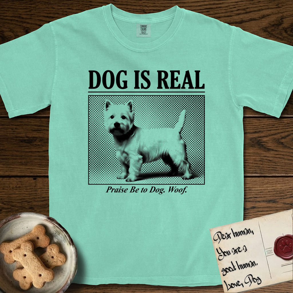 Dog is Real Westie T-Shirt flat lay in Island Reef, featuring Black halftone newspaper photo of a white Westie with upright ears and tail standing in profile with head turned to the camera, under the headline DOG IS REAL, with the caption Praise Be to Dog. Woof..