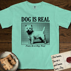 Dog is Real Westie T-Shirt flat lay in Island Reef, featuring Black halftone newspaper photo of a white Westie with upright ears and tail standing in profile with head turned to the camera, under the headline DOG IS REAL, with the caption Praise Be to Dog. Woof..