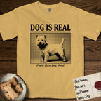 Dog is Real Westie T-Shirt flat lay in Mustard, featuring Black halftone newspaper photo of a white Westie with upright ears and tail standing in profile with head turned to the camera, under the headline DOG IS REAL, with the caption Praise Be to Dog. Woof..
