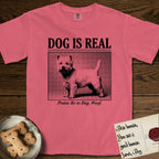 Dog is Real Westie T-Shirt flat lay in Watermelon, featuring Black halftone newspaper photo of a white Westie with upright ears and tail standing in profile with head turned to the camera, under the headline DOG IS REAL, with the caption Praise Be to Dog. Woof..