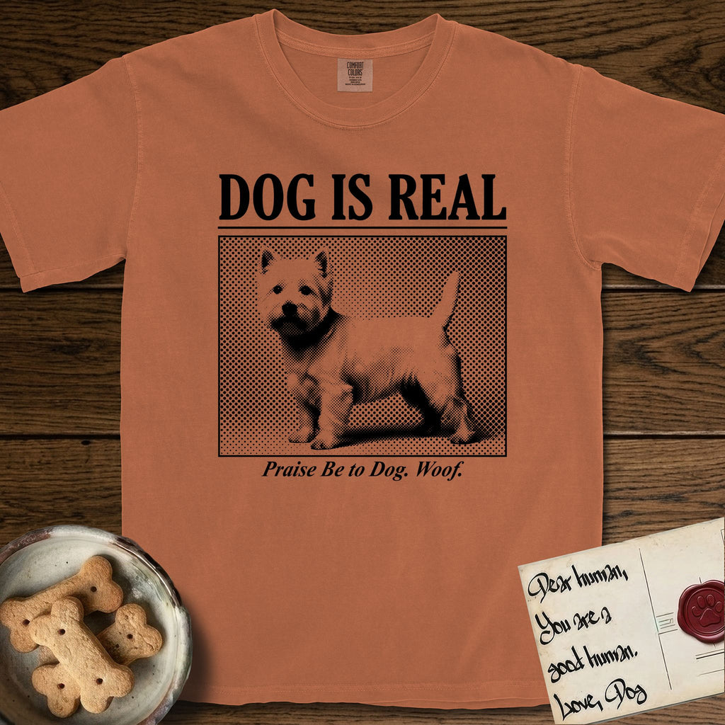 Dog is Real Westie T-Shirt flat lay in Yam, featuring Black halftone newspaper photo of a white Westie with upright ears and tail standing in profile with head turned to the camera, under the headline DOG IS REAL, with the caption Praise Be to Dog. Woof..