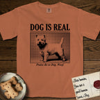 Dog is Real Westie T-Shirt flat lay in Yam, featuring Black halftone newspaper photo of a white Westie with upright ears and tail standing in profile with head turned to the camera, under the headline DOG IS REAL, with the caption Praise Be to Dog. Woof..