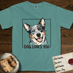 Dog Loves You Australian Cattle Dog T-Shirt flat lay in Blue Spruce, featuring Ink and watercolor portrait of a smiling blue Australian Cattle Dog with a speckled coat, tan eyebrows and upright ears, head tilted inside a black frame above hand-lettered text reading DOG LOVES YOU.
