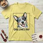 Dog Loves You Australian Cattle Dog T-Shirt flat lay in Cornsilk, featuring Ink and watercolor portrait of a smiling blue Australian Cattle Dog with a speckled coat, tan eyebrows and upright ears, head tilted inside a black frame above hand-lettered text reading DOG LOVES YOU.