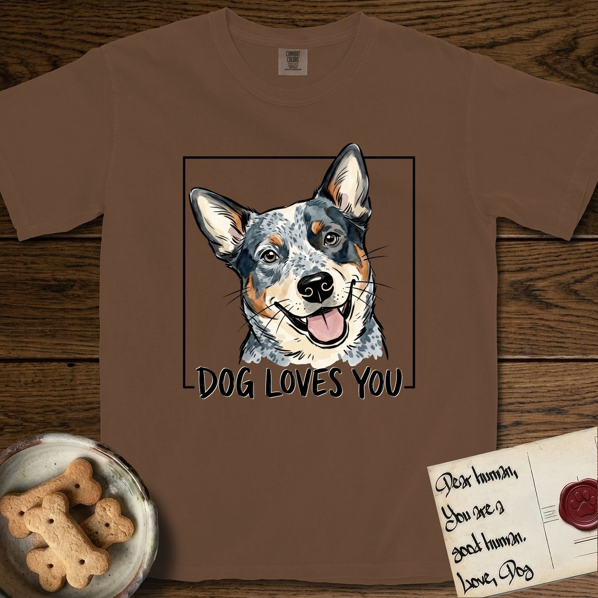 Dog Loves You Australian Cattle Dog T-Shirt flat lay in Espresso, featuring Ink and watercolor portrait of a smiling blue Australian Cattle Dog with a speckled coat, tan eyebrows and upright ears, head tilted inside a black frame above hand-lettered text reading DOG LOVES YOU.