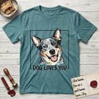 Dog Loves You Australian Cattle Dog T-Shirt flat lay in Heather Galapagos Blue, featuring Ink and watercolor portrait of a smiling blue Australian Cattle Dog with a speckled coat, tan eyebrows and upright ears, head tilted inside a black frame above hand-lettered text reading DOG LOVES YOU.