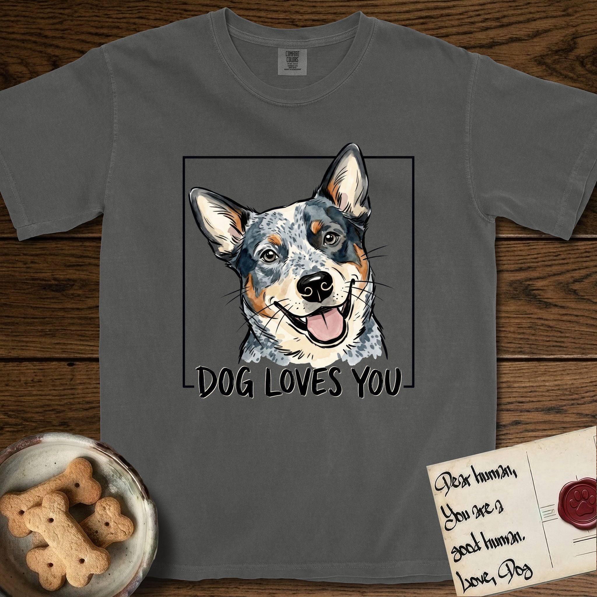 Dog Loves You Australian Cattle Dog T-Shirt flat lay in Pepper, featuring Ink and watercolor portrait of a smiling blue Australian Cattle Dog with a speckled coat, tan eyebrows and upright ears, head tilted inside a black frame above hand-lettered text reading DOG LOVES YOU.