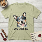 Dog Loves You Australian Cattle Dog T-Shirt flat lay in Pistachio, featuring Ink and watercolor portrait of a smiling blue Australian Cattle Dog with a speckled coat, tan eyebrows and upright ears, head tilted inside a black frame above hand-lettered text reading DOG LOVES YOU.