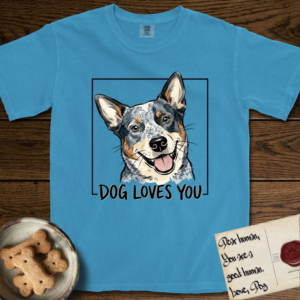 Dog Loves You Australian Cattle Dog T-Shirt flat lay in Royal Caribe, featuring Ink and watercolor portrait of a smiling blue Australian Cattle Dog with a speckled coat, tan eyebrows and upright ears, head tilted inside a black frame above hand-lettered text reading DOG LOVES YOU.