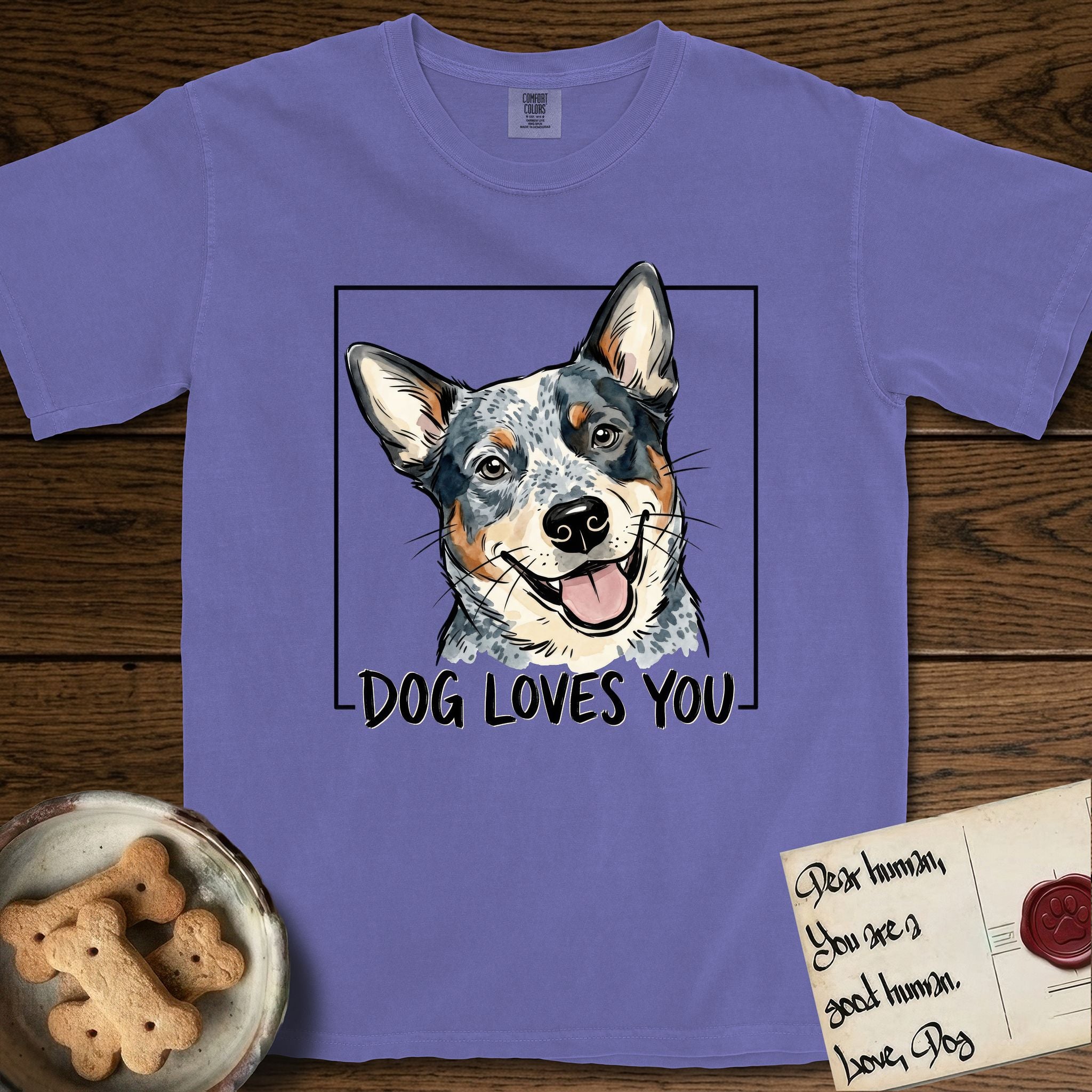Dog Loves You Australian Cattle Dog T-Shirt flat lay in Violet, featuring Ink and watercolor portrait of a smiling blue Australian Cattle Dog with a speckled coat, tan eyebrows and upright ears, head tilted inside a black frame above hand-lettered text reading DOG LOVES YOU.