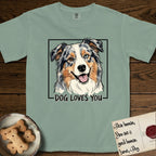Dog Loves You Australian Shepherd T-Shirt flat lay in Bay, featuring Ink and watercolor portrait of a smiling blue merle Australian Shepherd with one brown eye and one blue eye and a cream blaze, head tilted inside a black frame above hand-lettered text reading DOG LOVES YOU.