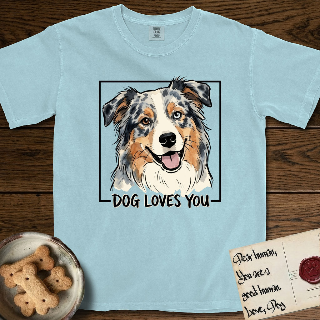 Dog Loves You Australian Shepherd T-Shirt flat lay in Chambray, featuring Ink and watercolor portrait of a smiling blue merle Australian Shepherd with one brown eye and one blue eye and a cream blaze, head tilted inside a black frame above hand-lettered text reading DOG LOVES YOU.