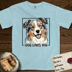 Dog Loves You Australian Shepherd T-Shirt flat lay in Chambray, featuring Ink and watercolor portrait of a smiling blue merle Australian Shepherd with one brown eye and one blue eye and a cream blaze, head tilted inside a black frame above hand-lettered text reading DOG LOVES YOU.