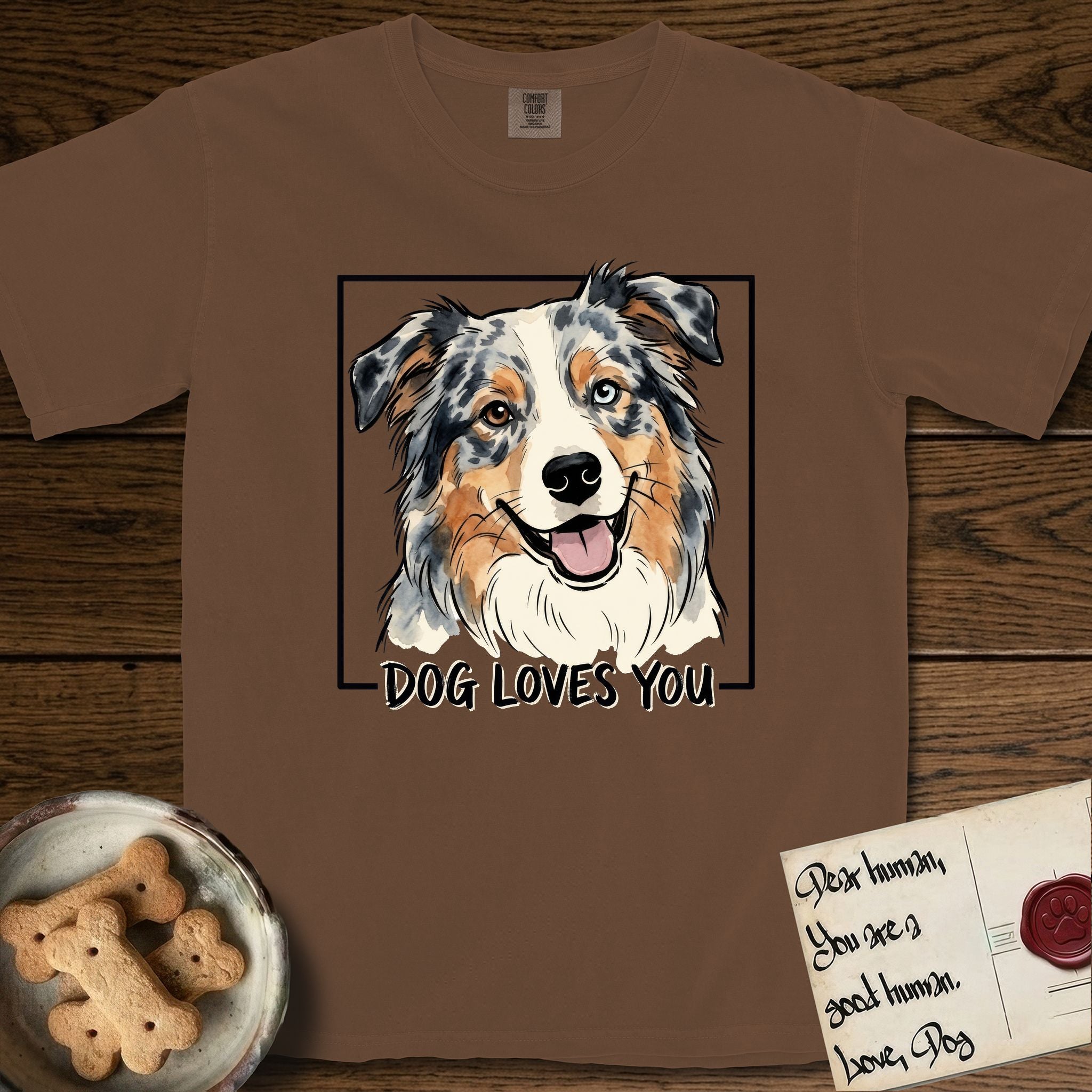 Dog Loves You Australian Shepherd T-Shirt flat lay in Espresso, featuring Ink and watercolor portrait of a smiling blue merle Australian Shepherd with one brown eye and one blue eye and a cream blaze, head tilted inside a black frame above hand-lettered text reading DOG LOVES YOU.