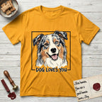 Dog Loves You Australian Shepherd T-Shirt flat lay in Gold, featuring Ink and watercolor portrait of a smiling blue merle Australian Shepherd with one brown eye and one blue eye and a cream blaze, head tilted inside a black frame above hand-lettered text reading DOG LOVES YOU.