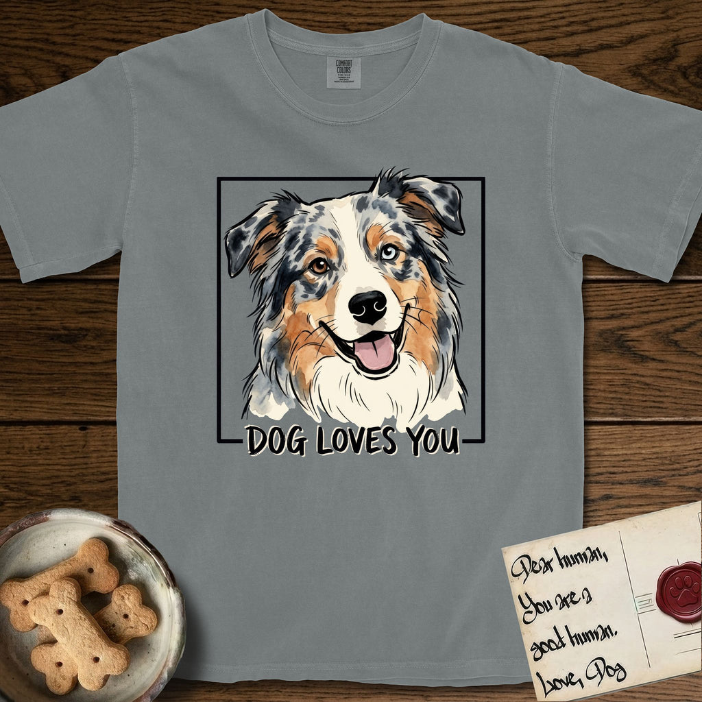 Dog Loves You Australian Shepherd T-Shirt flat lay in Granite, featuring Ink and watercolor portrait of a smiling blue merle Australian Shepherd with one brown eye and one blue eye and a cream blaze, head tilted inside a black frame above hand-lettered text reading DOG LOVES YOU.