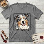 Dog Loves You Australian Shepherd T-Shirt flat lay in Graphite Heather, featuring Ink and watercolor portrait of a smiling blue merle Australian Shepherd with one brown eye and one blue eye and a cream blaze, head tilted inside a black frame above hand-lettered text reading DOG LOVES YOU.