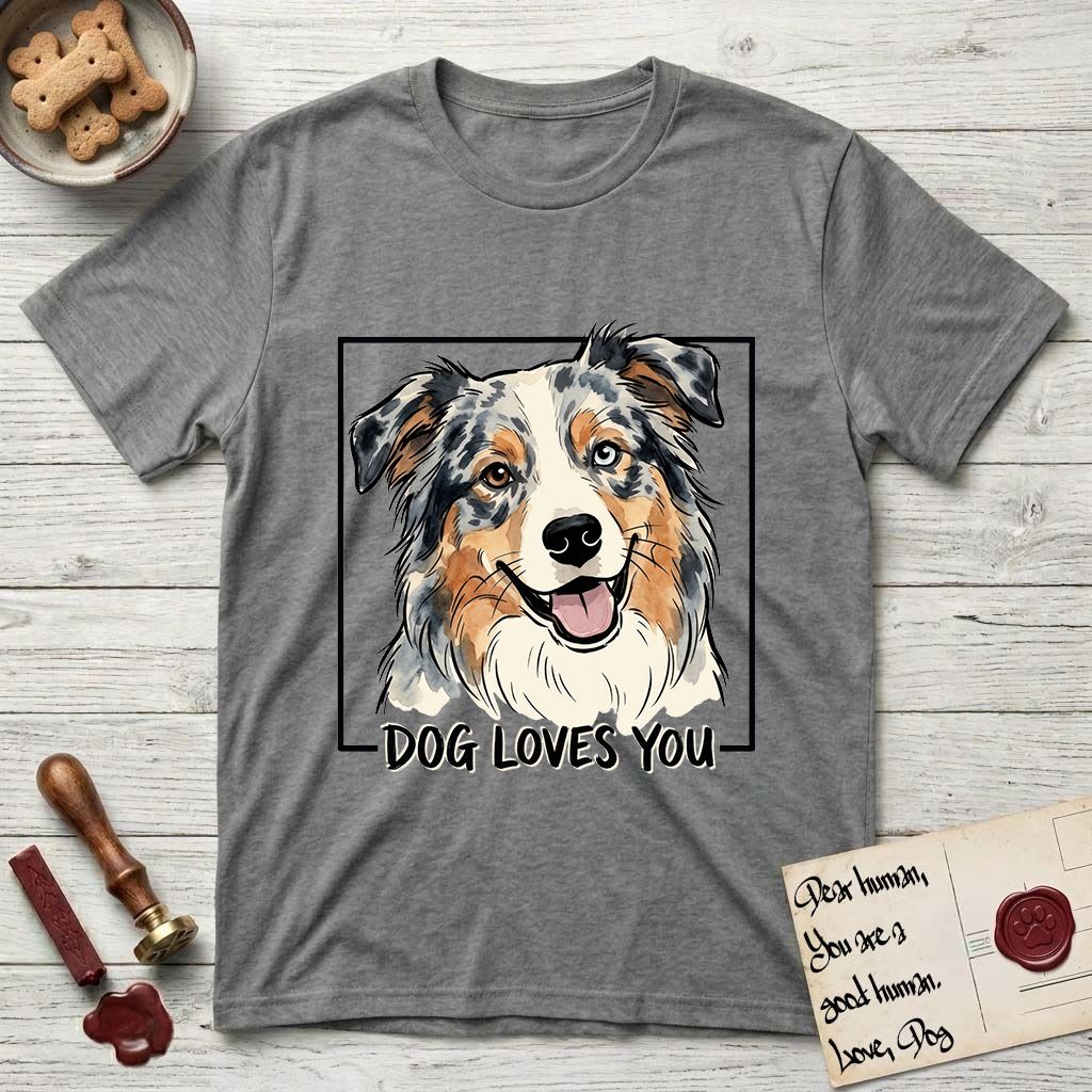 Dog Loves You Australian Shepherd T-Shirt flat lay in Graphite Heather, featuring Ink and watercolor portrait of a smiling blue merle Australian Shepherd with one brown eye and one blue eye and a cream blaze, head tilted inside a black frame above hand-lettered text reading DOG LOVES YOU.