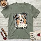 Dog Loves You Australian Shepherd T-Shirt flat lay in Sage, featuring Ink and watercolor portrait of a smiling blue merle Australian Shepherd with one brown eye and one blue eye and a cream blaze, head tilted inside a black frame above hand-lettered text reading DOG LOVES YOU.