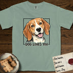 Dog Loves You Beagle T-Shirt flat lay in Bay, featuring Ink and watercolor portrait of a smiling tricolor Beagle with long hanging ears and a cream blaze, head tilted inside a black frame above hand-lettered text reading DOG LOVES YOU.