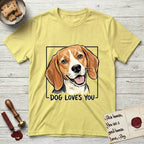 Dog Loves You Beagle T-Shirt flat lay in Cornsilk, featuring Ink and watercolor portrait of a smiling tricolor Beagle with long hanging ears and a cream blaze, head tilted inside a black frame above hand-lettered text reading DOG LOVES YOU.