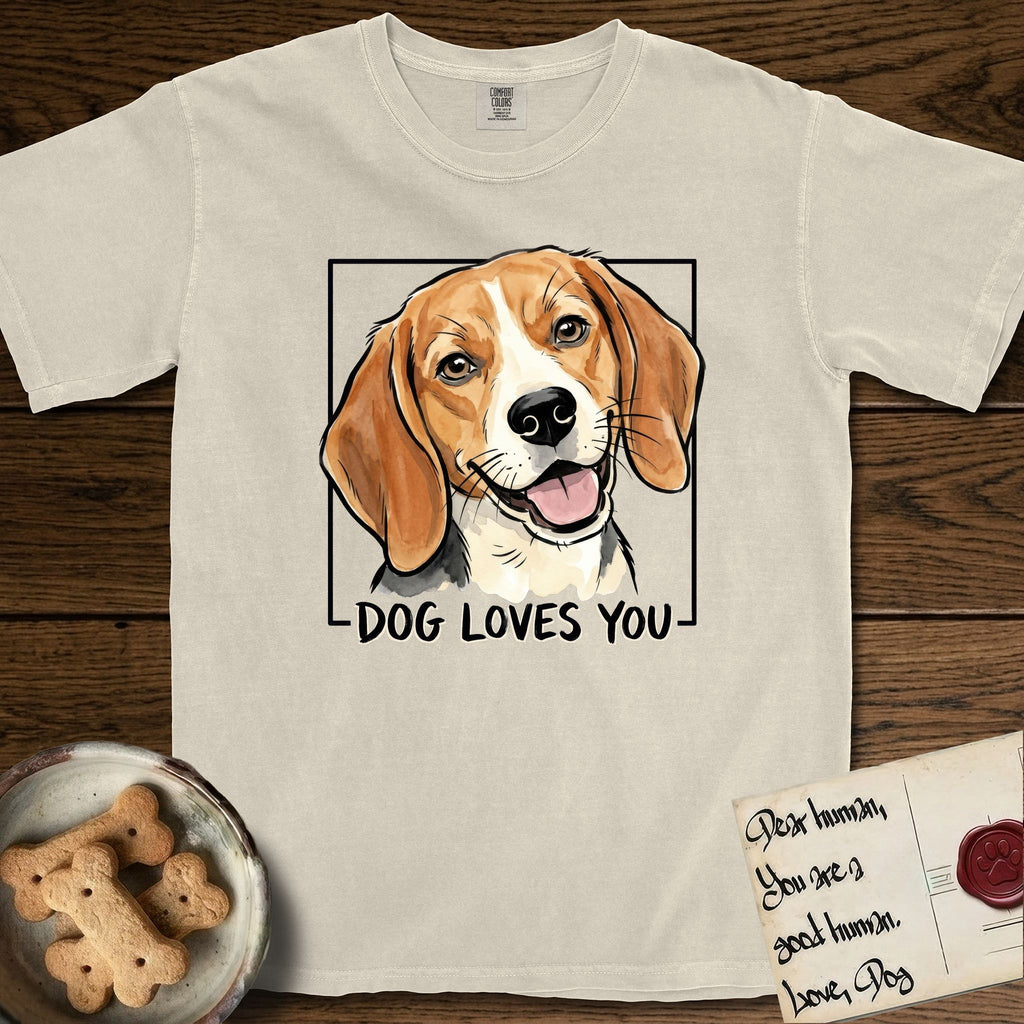 Dog Loves You Beagle T-Shirt flat lay in Ivory, featuring Ink and watercolor portrait of a smiling tricolor Beagle with long hanging ears and a cream blaze, head tilted inside a black frame above hand-lettered text reading DOG LOVES YOU.