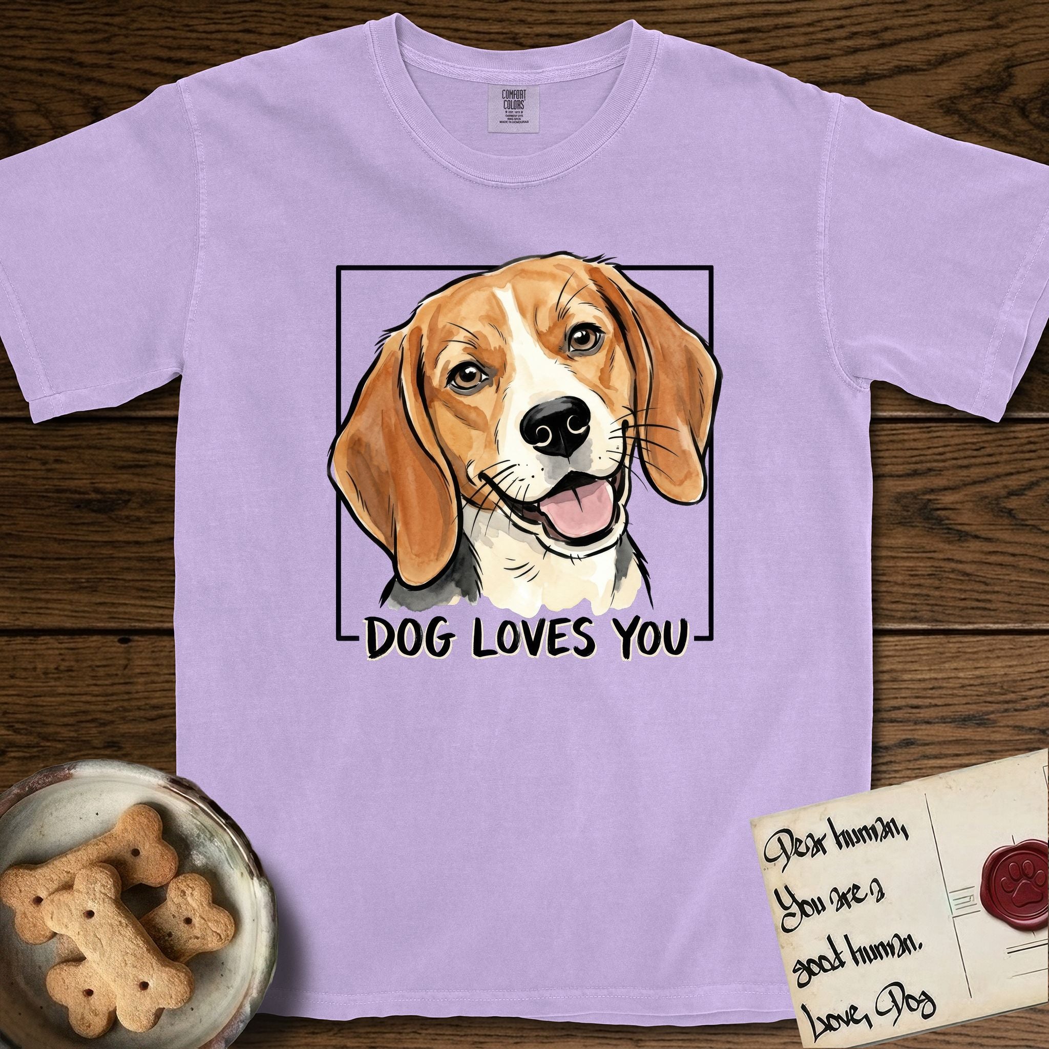 Dog Loves You Beagle T-Shirt flat lay in Orchid, featuring Ink and watercolor portrait of a smiling tricolor Beagle with long hanging ears and a cream blaze, head tilted inside a black frame above hand-lettered text reading DOG LOVES YOU.