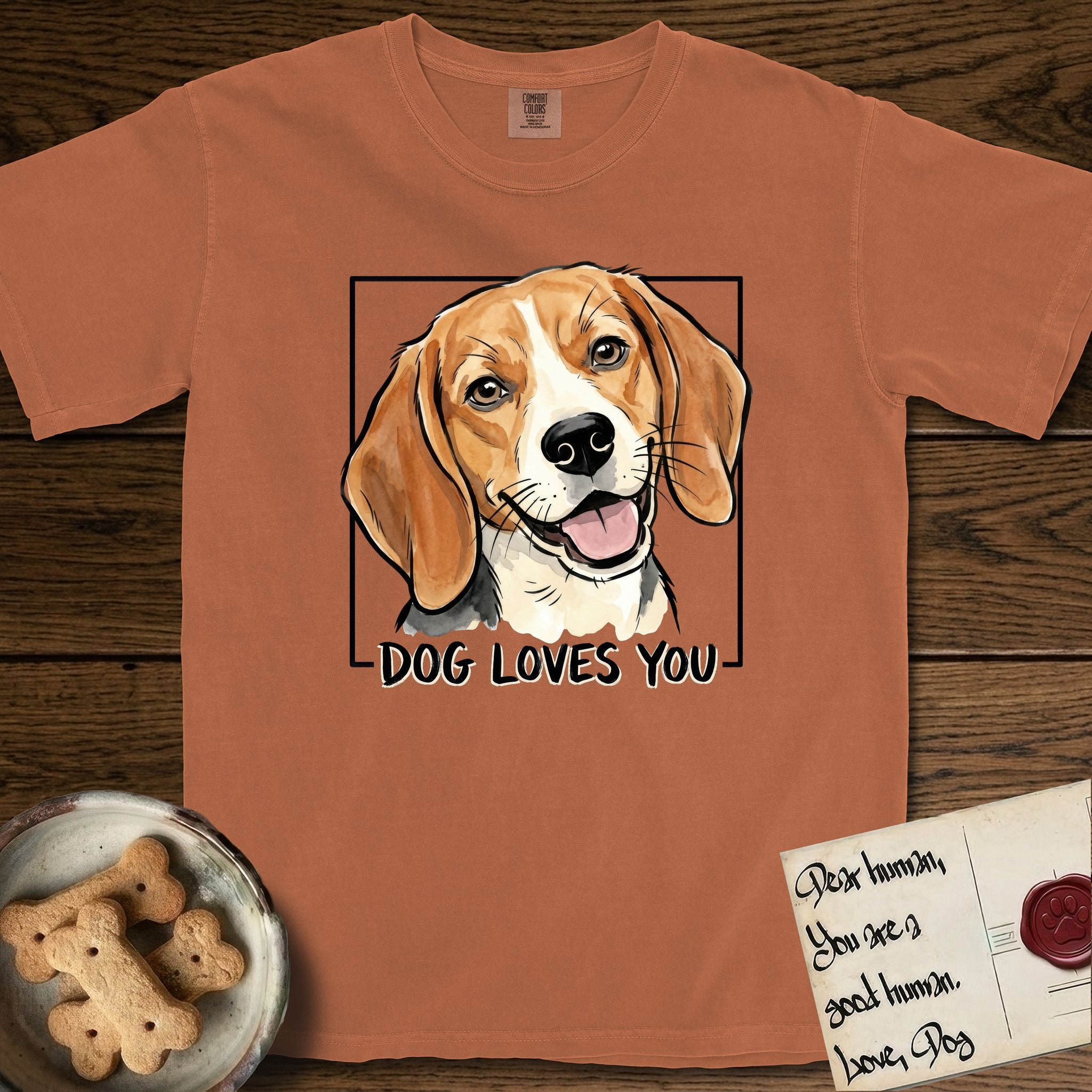 Dog Loves You Beagle T-Shirt flat lay in Yam, featuring Ink and watercolor portrait of a smiling tricolor Beagle with long hanging ears and a cream blaze, head tilted inside a black frame above hand-lettered text reading DOG LOVES YOU.