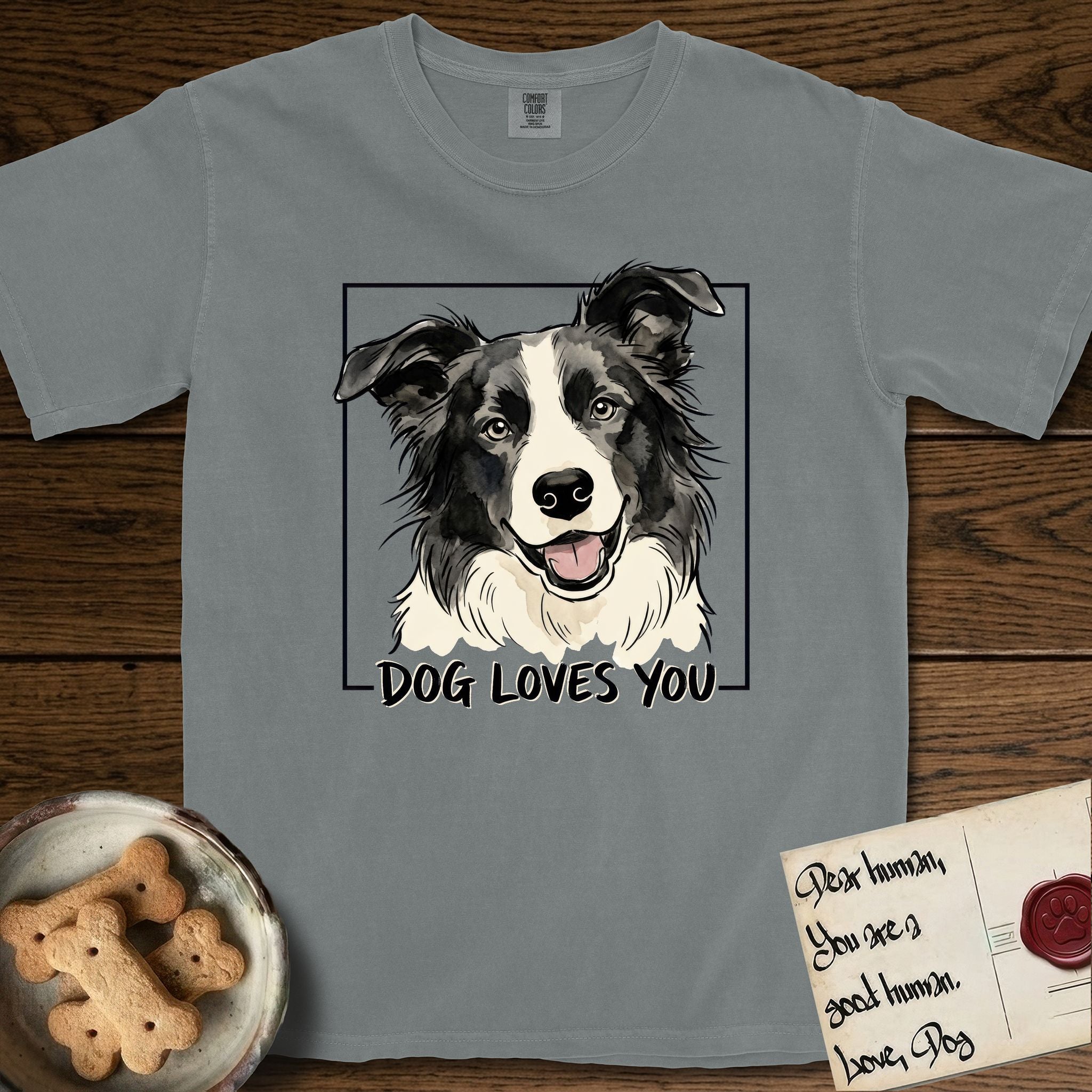 Dog Loves You Border Collie T-Shirt flat lay in Granite, featuring Ink and watercolor portrait of a smiling black and white Border Collie with a cream blaze and semi-erect ears, head tilted inside a black frame above hand-lettered text reading DOG LOVES YOU.