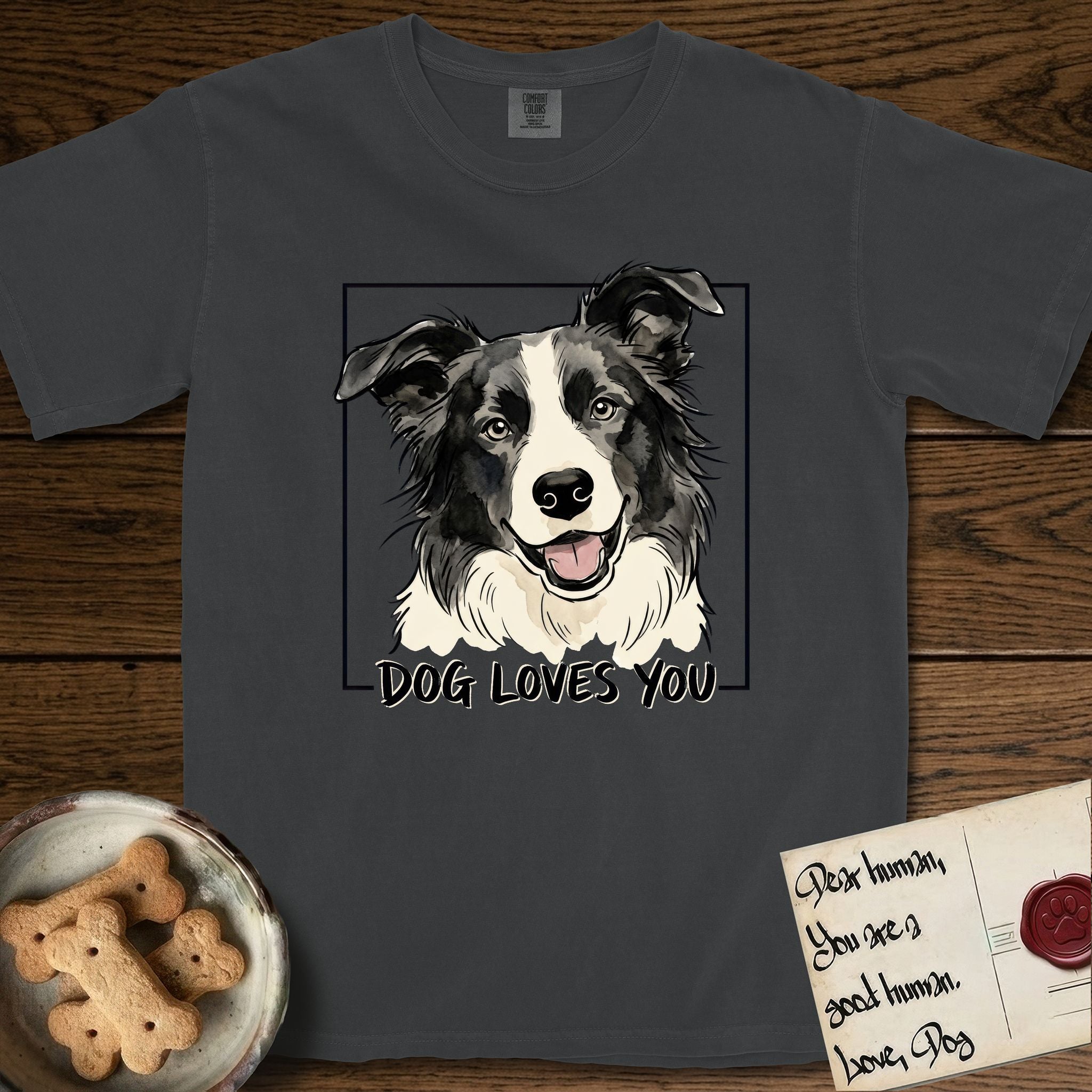 Dog Loves You Border Collie T-Shirt flat lay in Graphite, featuring Ink and watercolor portrait of a smiling black and white Border Collie with a cream blaze and semi-erect ears, head tilted inside a black frame above hand-lettered text reading DOG LOVES YOU.