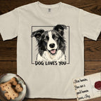 Dog Loves You Border Collie T-Shirt flat lay in Ivory, featuring Ink and watercolor portrait of a smiling black and white Border Collie with a cream blaze and semi-erect ears, head tilted inside a black frame above hand-lettered text reading DOG LOVES YOU.