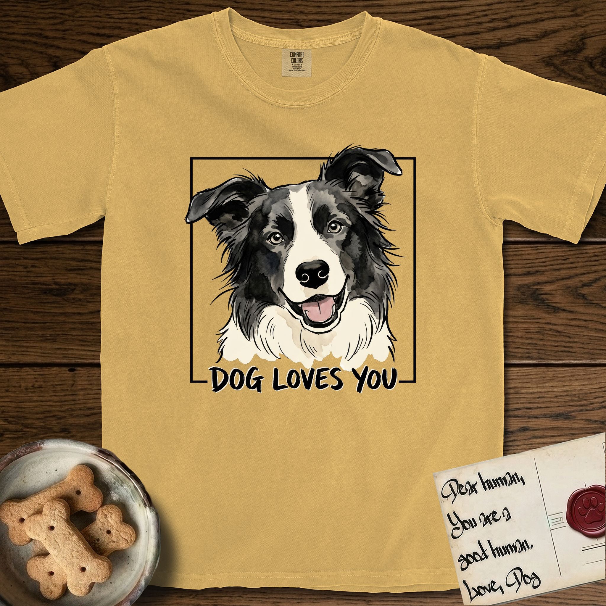 Dog Loves You Border Collie T-Shirt flat lay in Mustard, featuring Ink and watercolor portrait of a smiling black and white Border Collie with a cream blaze and semi-erect ears, head tilted inside a black frame above hand-lettered text reading DOG LOVES YOU.