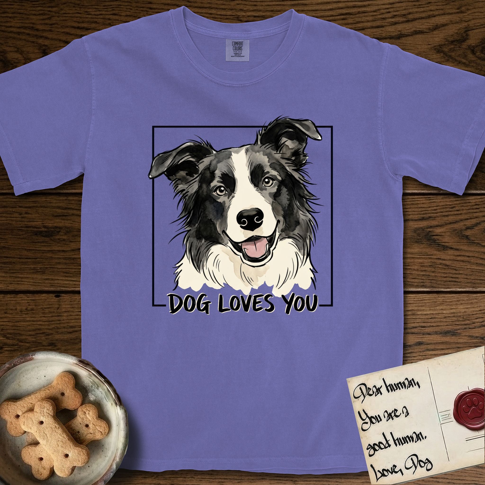 Dog Loves You Border Collie T-Shirt flat lay in Violet, featuring Ink and watercolor portrait of a smiling black and white Border Collie with a cream blaze and semi-erect ears, head tilted inside a black frame above hand-lettered text reading DOG LOVES YOU.