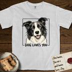 Dog Loves You Border Collie T-Shirt flat lay in White, featuring Ink and watercolor portrait of a smiling black and white Border Collie with a cream blaze and semi-erect ears, head tilted inside a black frame above hand-lettered text reading DOG LOVES YOU.