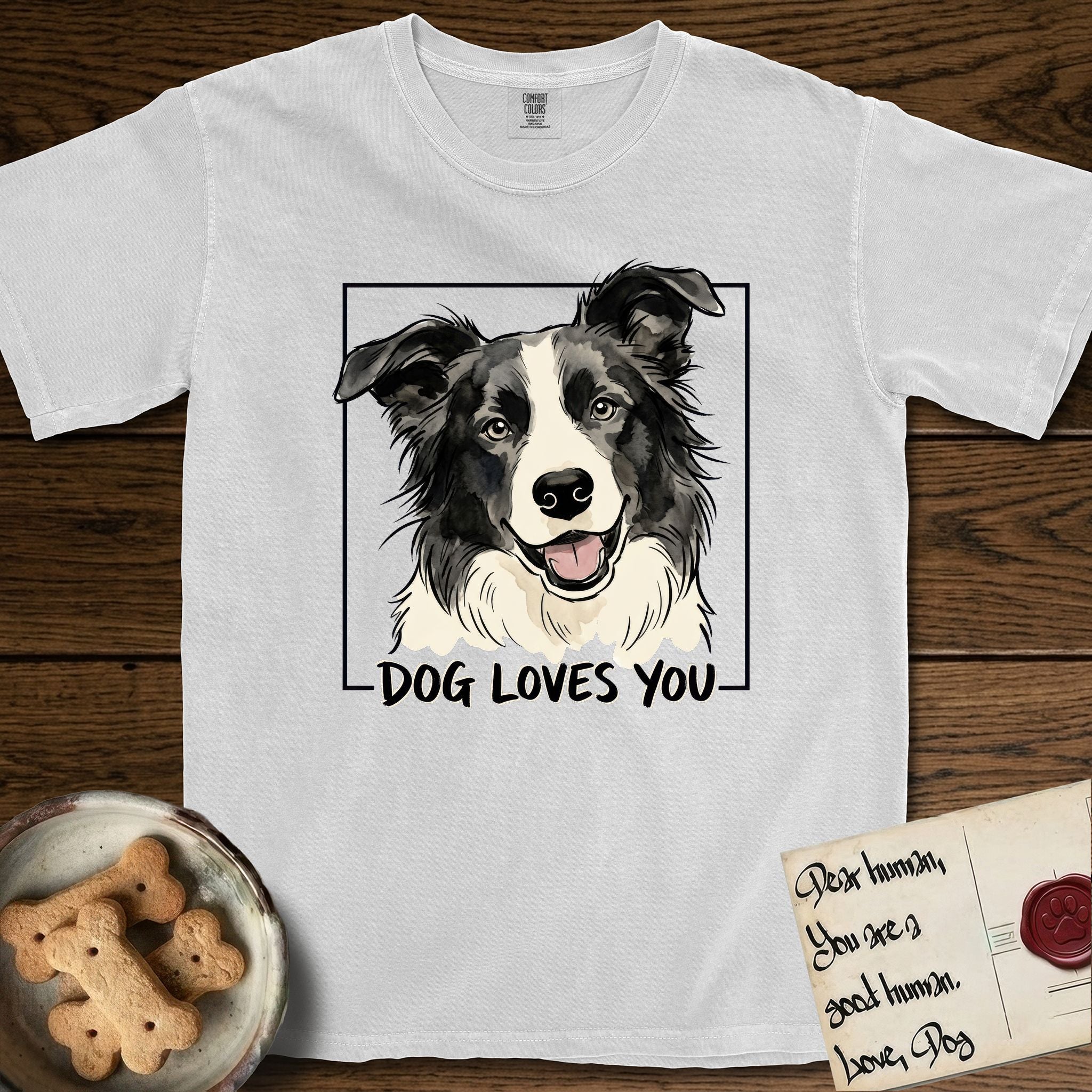 Dog Loves You Border Collie T-Shirt flat lay in White, featuring Ink and watercolor portrait of a smiling black and white Border Collie with a cream blaze and semi-erect ears, head tilted inside a black frame above hand-lettered text reading DOG LOVES YOU.