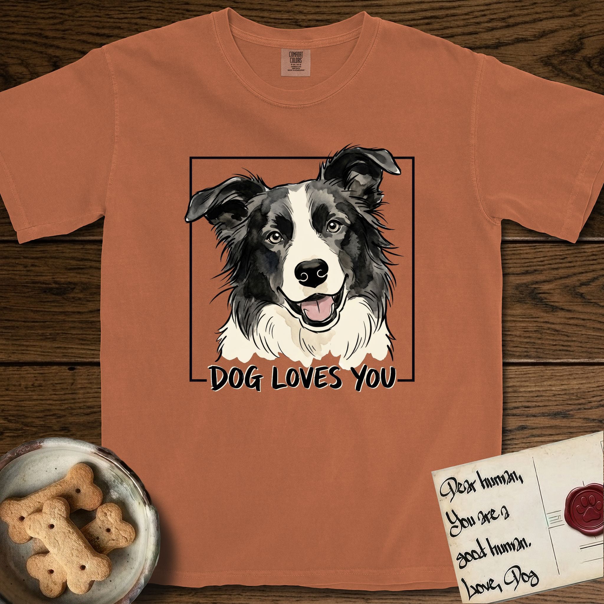 Dog Loves You Border Collie T-Shirt flat lay in Yam, featuring Ink and watercolor portrait of a smiling black and white Border Collie with a cream blaze and semi-erect ears, head tilted inside a black frame above hand-lettered text reading DOG LOVES YOU.